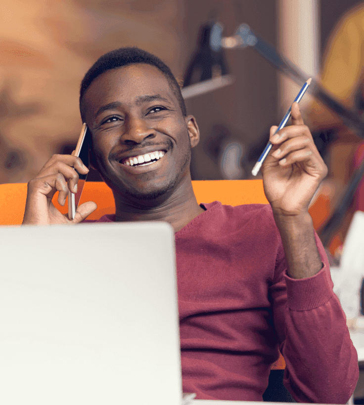 Um homem sorridente falando ao celular e usando o computador